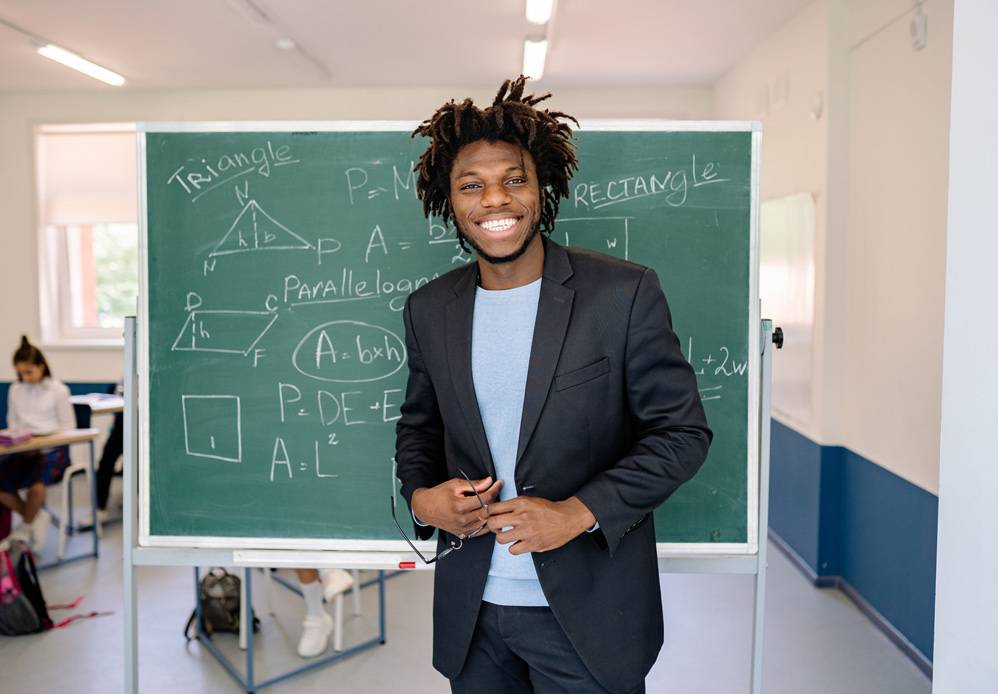 Male educator smiling in front of chalk board